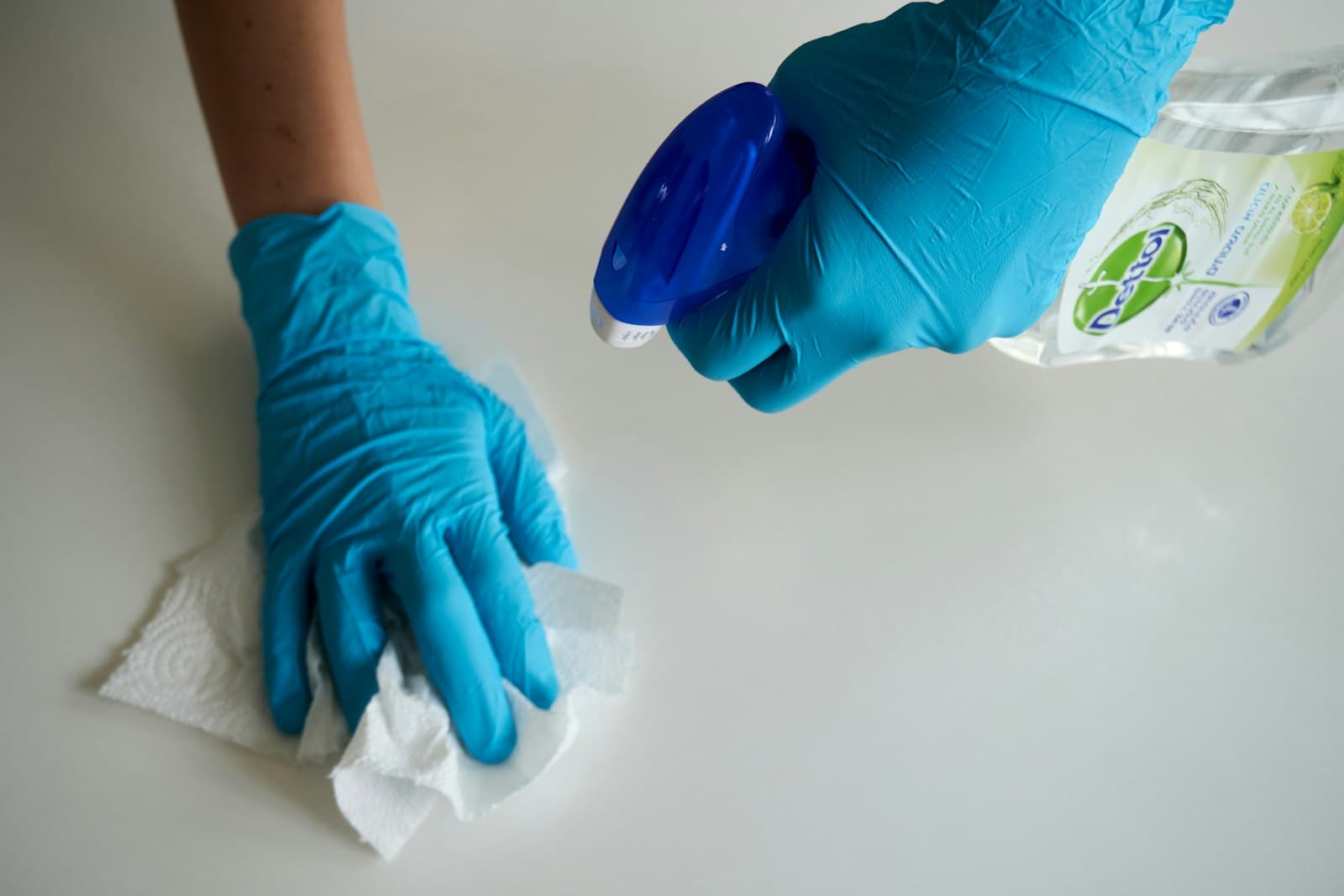 Cleaner in blue gloves wiping and disinfecting a white surface