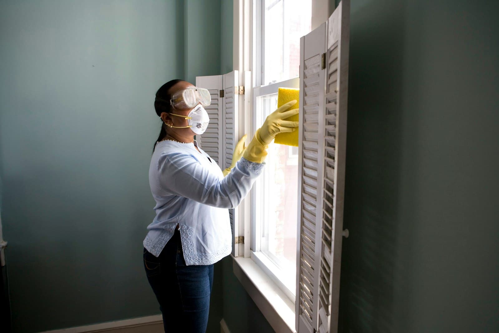 Professional cleaner in gloves wiping a window in a home